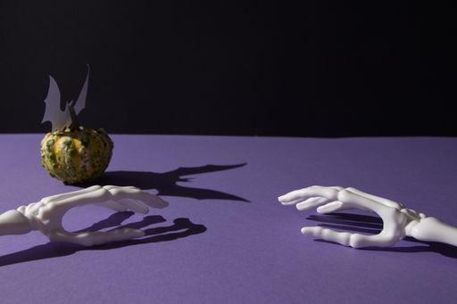 A pumpkin for Helloween and shadow of bat and hand bones on purple black background