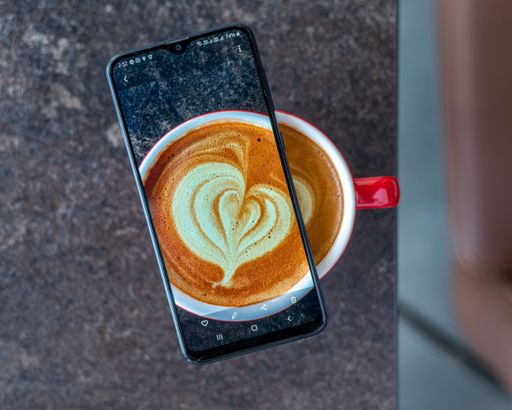 A top view of a transparent smartphone on a Cappuccino cup on a gray marble background