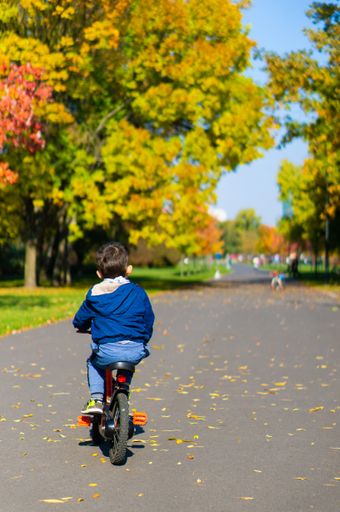 A vertical shot of a Caucasian boy riding a bicycle in the Jan Pawla park