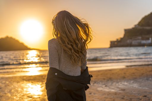 A female getting off her coat while walking toward the sea at sunset