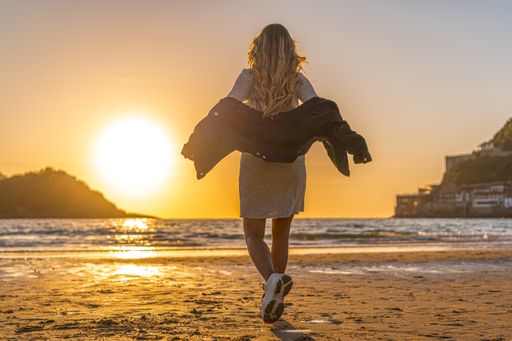 A female getting off her coat while walking toward the sea at sunset
