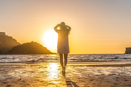 A young Colombian blonde female walking toward the sea at the beach of San Sebastian, Spain at sunset