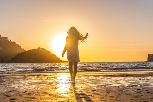 A young Colombian blonde female walking toward the sea at the beach of San Sebastian, Spain at sunset