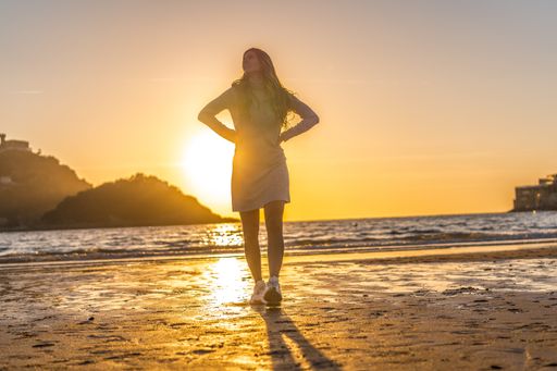 A beautiful young Colombian blonde in a grey dress on the beach at sunset in San Sebastian, Spain