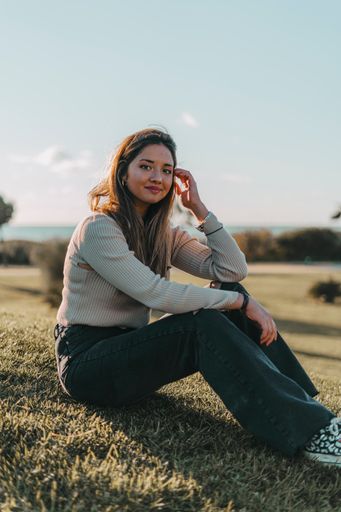 A pretty young Spanish brunette girl posing outdoors sitting on green grass on a sunny day