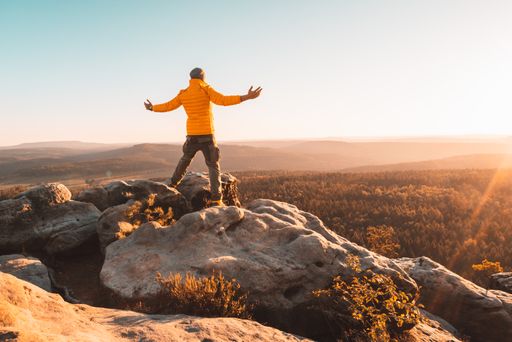 A back view of a young male hiker on the top of a rock with open arms admiring the view of nature