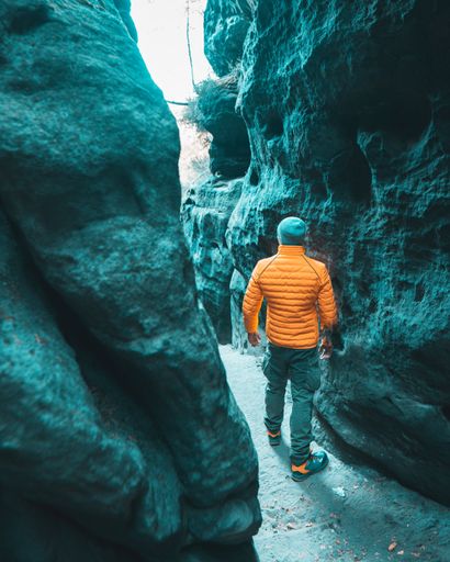 A back view of a young male traveler in winterwear standing between the walls of a cave