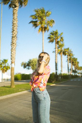 A caucasian blonde pretty girl posing in the park under the sun with a summer outfit