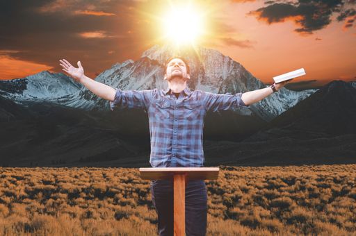 A person with open arms holding a bible with the mountain under the sunlight on the background