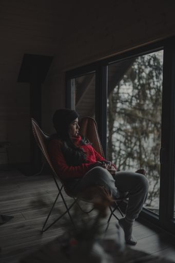 A vertical shot of a Hispanic woman in red pullover sitting on a butterfly chair and watching nature