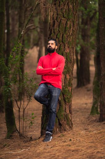 A vertical shot of a bearded Hispanic man leaning on a tree trunk in the forest