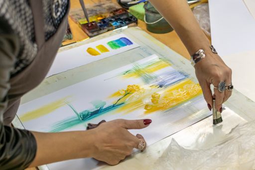 Cropped female hands of artist paint on white paper watercolor drawing with large brush. Artistic master class for young artists.
