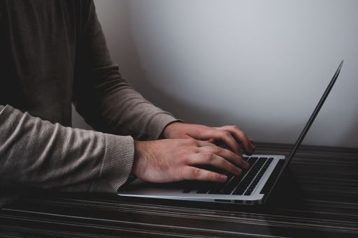 A male's hands typing on a laptop keyboard on a wooden table