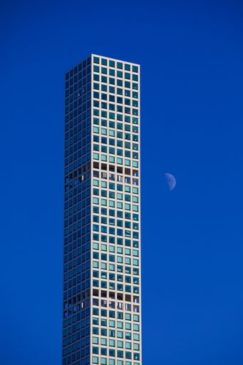 A vertical shot of the moon rising near a skyscraper in New York City