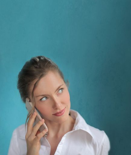A vertical picture of a blonde female in a white shirt talking by phone against a blue background