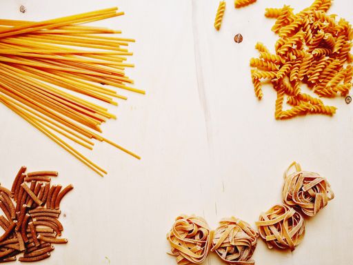 A flat lay with different pasta shapes placed on a wooden board, copy space in the middle