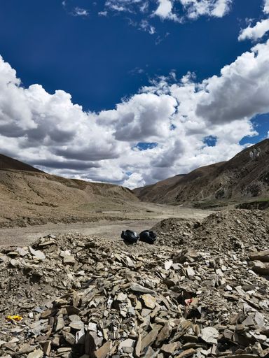 A vertical shot of two garbage bags on the rocks by a road with mountains and clouds in the background
