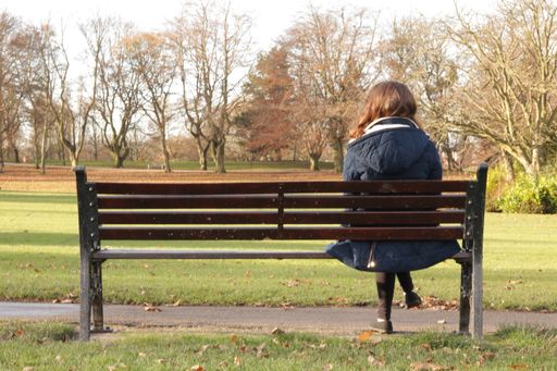 Woman with long brown hair sitting on the bench at the park
