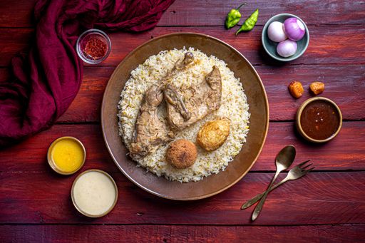 a top view of the famous Indian biryani dish including rice, chicken, vegetables and sauces on red wood table