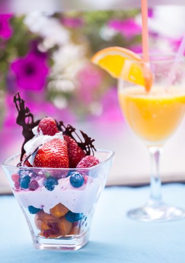 A vertical shot of vanilla ice cream with berries and fruits and a glass of orange juice