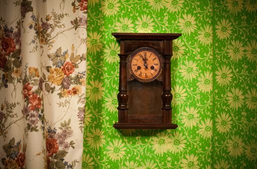 A closeup shot of an old vintage style wooden clock hanging on a green wall
