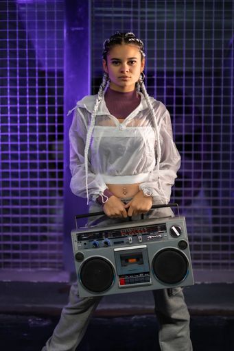 A vertical shot of a pretty Caucasian lady with piercings, braids, and a boombox - in the 80s style