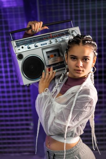 A vertical shot of a pretty Caucasian lady with piercings, braids, and a boombox - in the 80s style