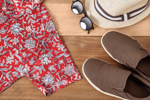 A pair of sneakers, a shirt, sunglasses and a hat on a wooden background