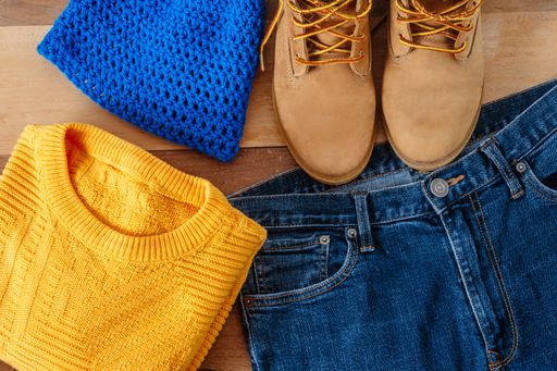 A pair of boots, jeans, a sweater and a hat on a wooden background