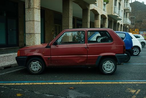 A side view of a Fiat Panda vintage Italian car with a damaged door parked in front of a building