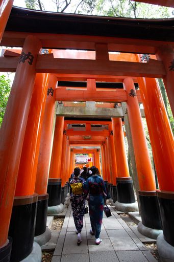 People walking in the orange entrance into the Fushimi Inari Shrine in Kyoto, Japan
