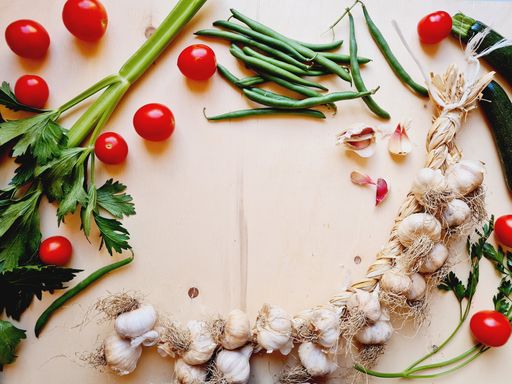 A top view of a garlic braid, Cherry tomatoes, beans, zucchini and celery on wooden table