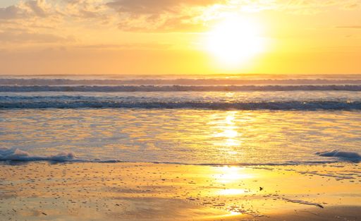 A beach surrounded by the wavy sea under the sunlight during a golden sunset - perfect for wallpapers