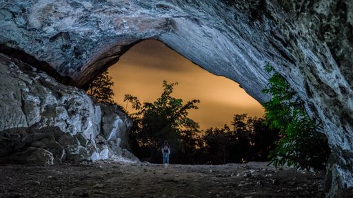 A person standing under the rocks surrounded by trees during the evening - cool for backgrounds