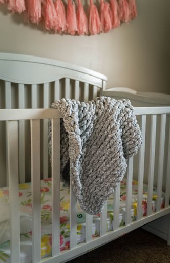 The interior of a cozy baby room with a white crib and soft custom made chunky blanket