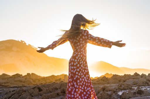 A view of a female with a red dress enjoying the sunset by the sea with her arms open