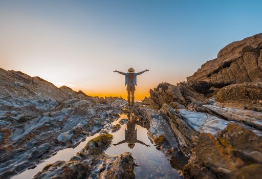 A beautiful view of a female standing on top of a cliff while enjoying the sunset by the sea