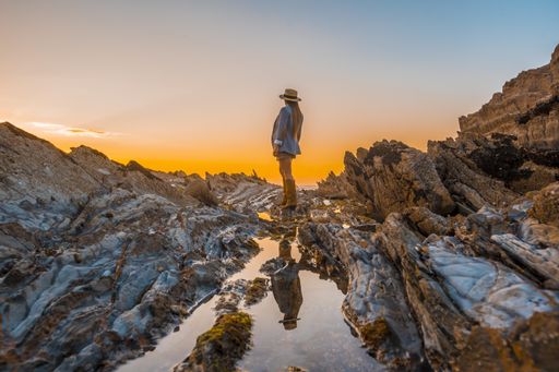 A beautiful view of a female standing on top of a cliff while enjoying the sunset by the sea