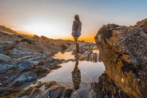A beautiful view of a female standing on top of a cliff while enjoying the sunset by the sea