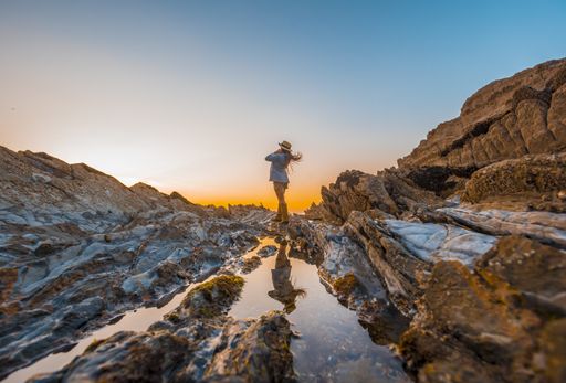 A beautiful view of a female standing on top of a cliff while enjoying the sunset by the sea