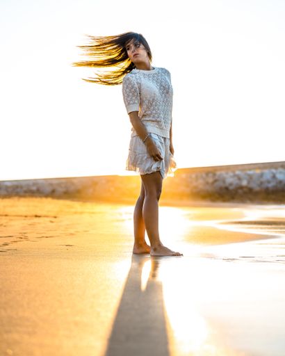 A vertical shot of a female wearing a white dress while walking on the beach during the sunset