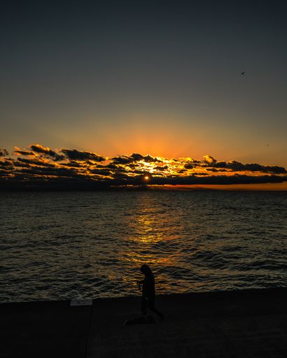 A vertical shot of a cloudy sunset sky over the Chicago Lake with a silhouette of a person walking with a dog