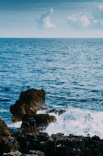 A vertical shot of rocks surrounded by the wavy sea under the sunlight and a blue sky at daytime