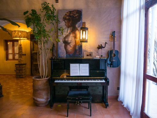 A black shiny acoustic guitar hanging next to a black piano in a room