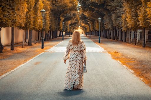 A closeup shot of a woman with beautiful long dress walking on the road among autumn trees