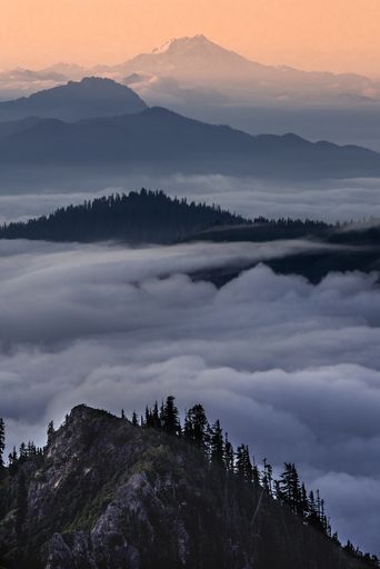 A vertical shot of mountains above the clouds with an orange sky in the background