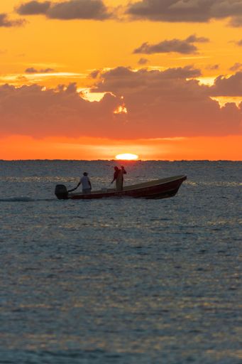 A vertical shot of gorgeous sunset with a foreground of the sea and silhouettes of people in a boat