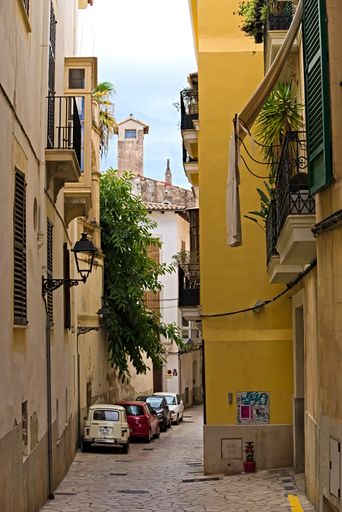 Palma, Mallorca, Spain - October 8th 2021: Cars park in colorful side street, old houses, one with yellow wall, balconies and plants hanging