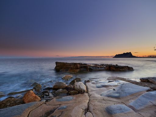 A scenic view of rocks coming out of water under a sunset-colored sky in a long exposure - wallpaper