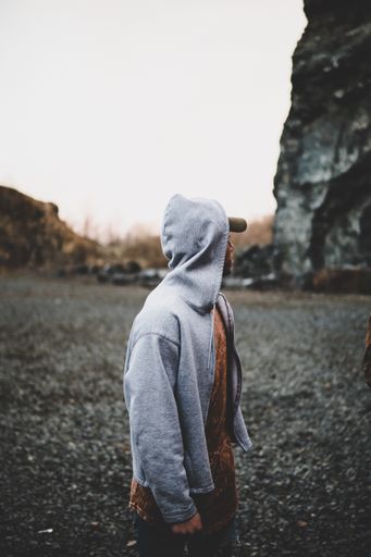 A selective focus photography of male in a gray hoodie standing near a rock formation